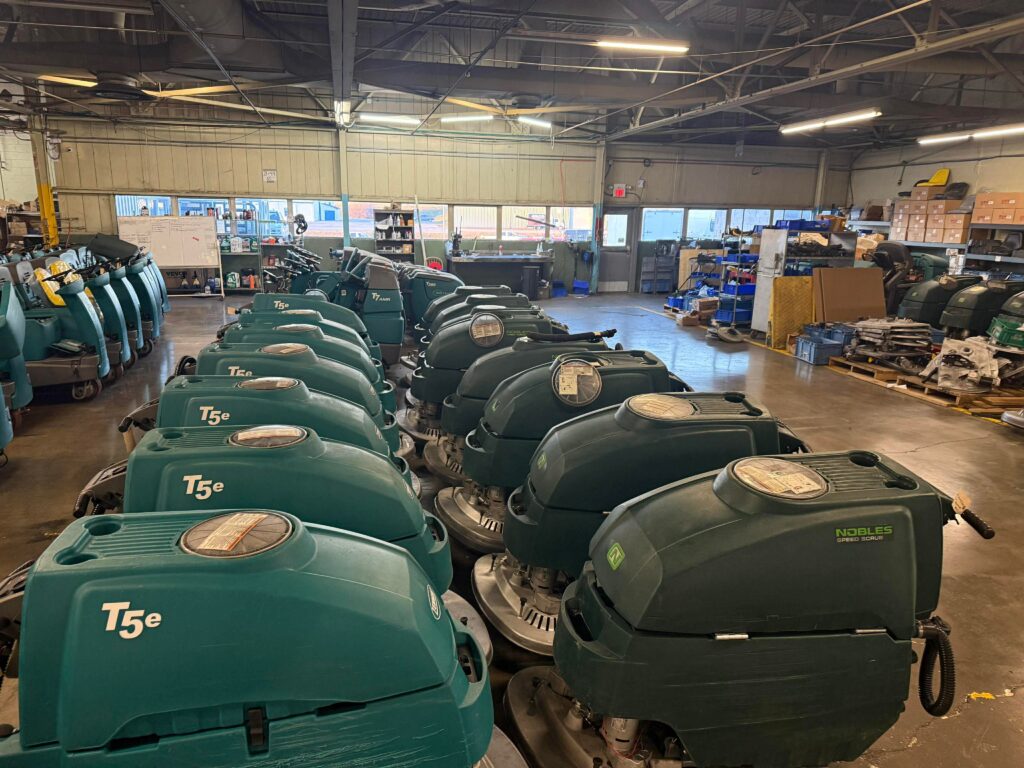 PowerKleen warehouse with multiple Tennant and Nobles commercial floor scrubber machines lined up for service, sales, and industrial cleaning applications.