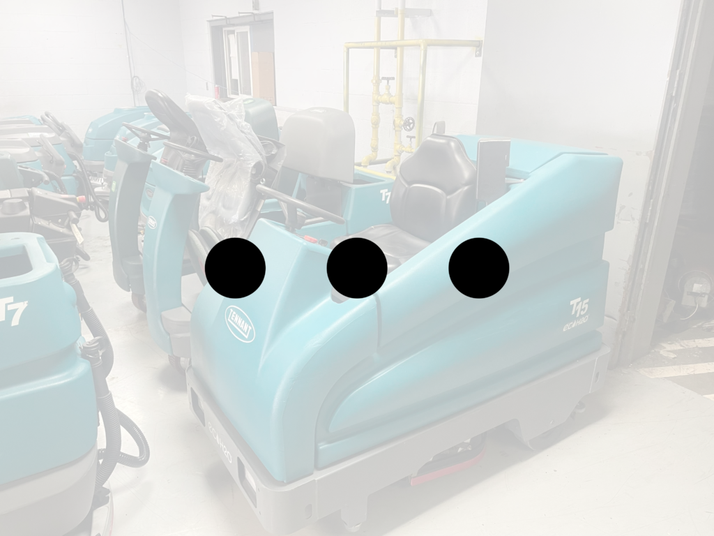 More ride-on floor scrubber machine parked inside a commercial cleaning equipment warehouse with multiple industrial floor scrubbers in the background.
