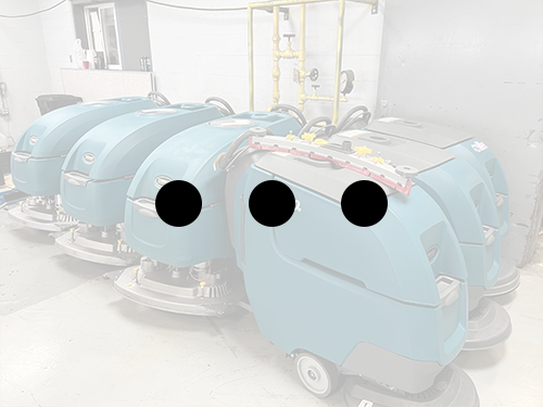 PowerKleen Tennant walk-behind floor scrubber machines lined up in a commercial equipment warehouse.